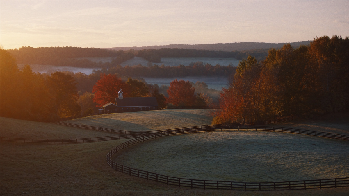 Kentucky horse country with black plank fences and a barn in autumn mist at sunrise